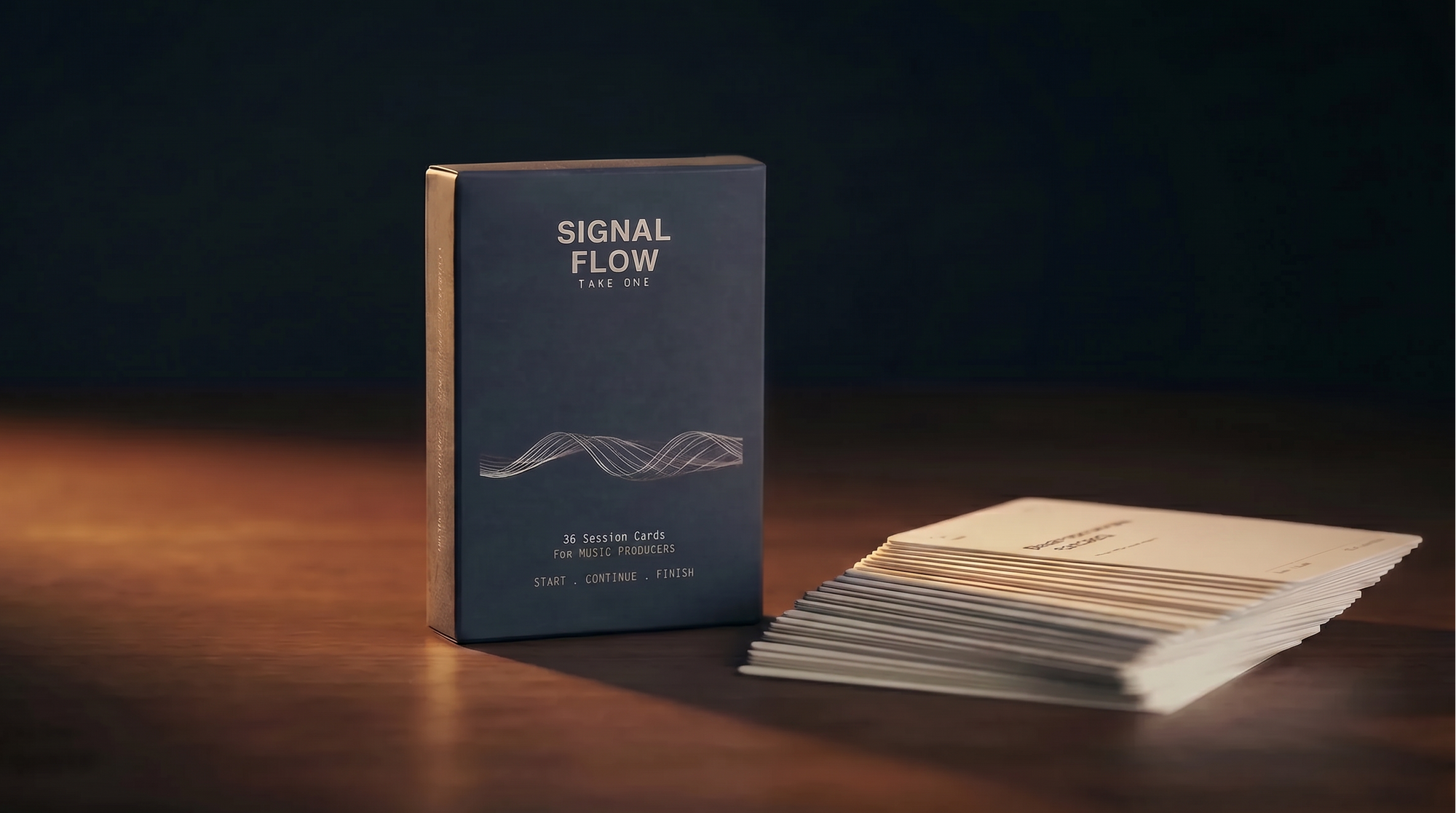A boxed card deck titled 'SIGNAL FLOW' standing upright on a wooden surface, with a fanned stack of cream-colored cards beside it against a dark background.